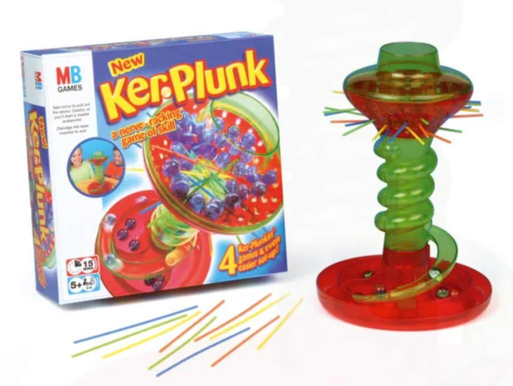 The game KerPluck. Shown here are the game box and the game itself. A plastic tower, some straws and marbles. The aim of the game is to pull out the straws and not allow the marbles to fall. The winner is the player with the least marbles at the end.