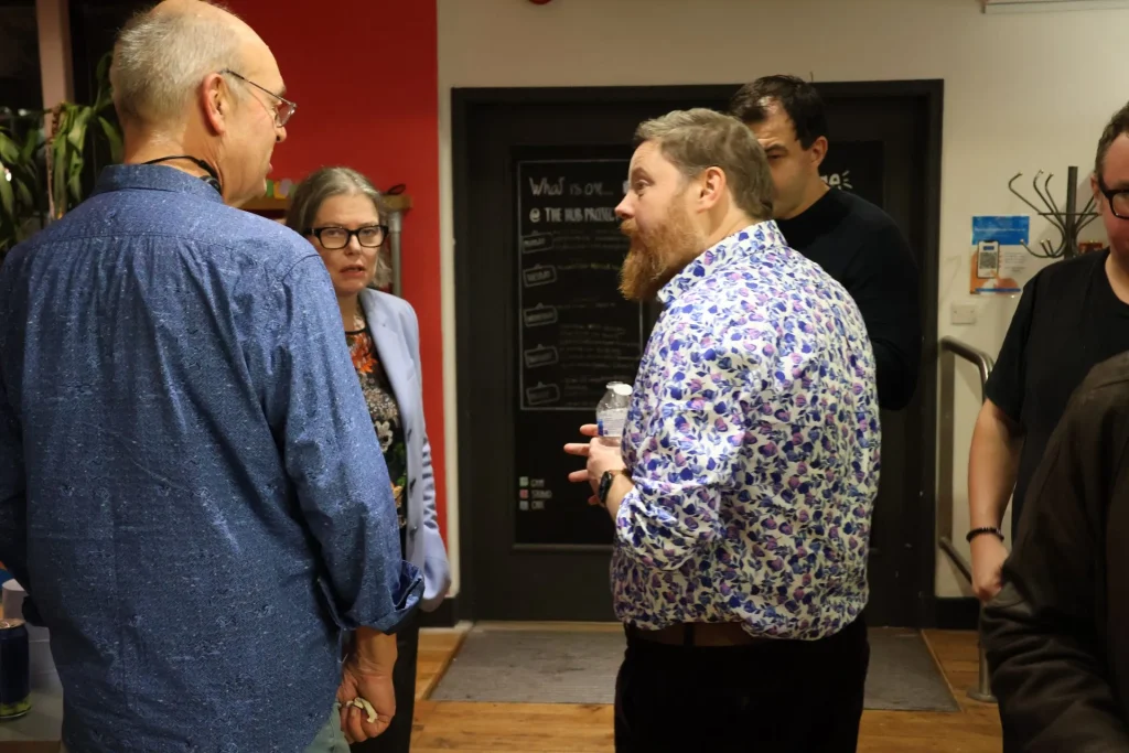 A group of people engaged in conversation during a networking event, with one individual wearing a floral shirt and holding a water bottle.