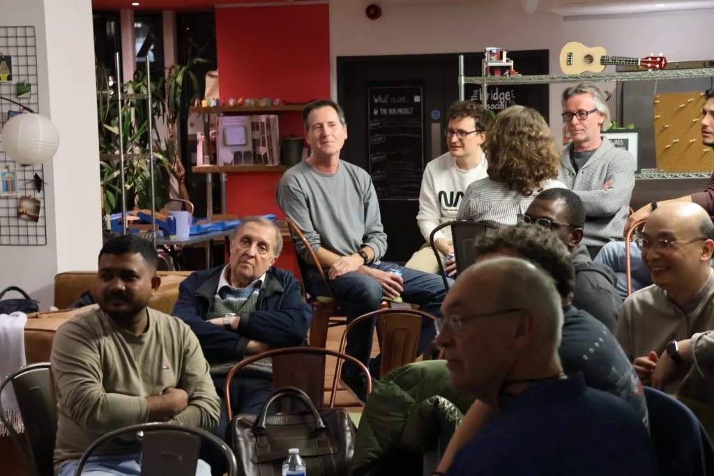 A group of attendees engaged in conversation during a presentation at an event, with a relaxed and attentive atmosphere.