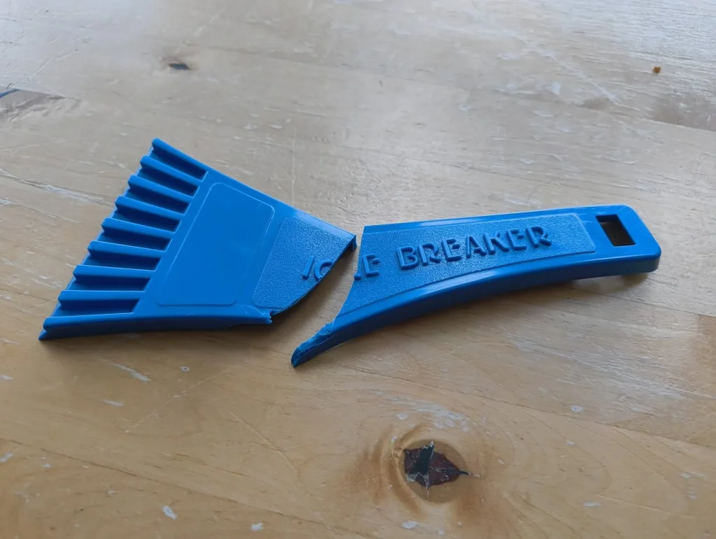 A broken blue plastic ice scraper with a jagged edge on a wooden surface.