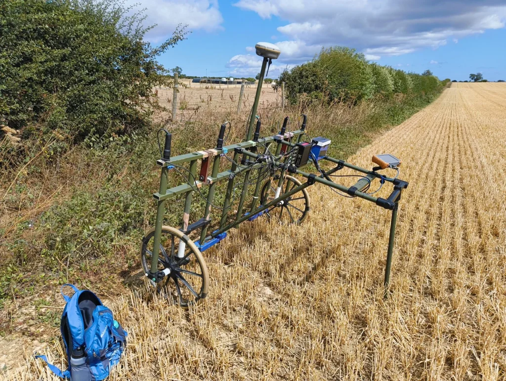 A field with a homemade trolley, various attachments, and a blue backpack resting beside it.
